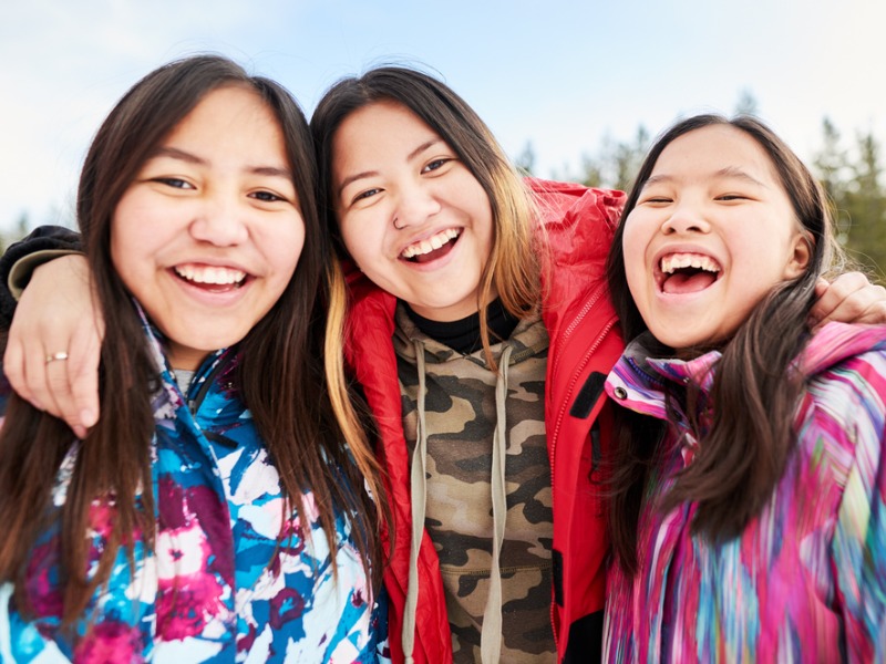 Trois jeunes autochtones souriantes sur un fonds hivernal.